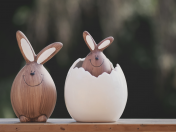 Osterhasendekoration: Ein brauner Keramikhase sitzt neben einem weißen, aufgebrochenen Keramikei. Aus dem Ei guckt ein kleinerer brauner Keramikhase.